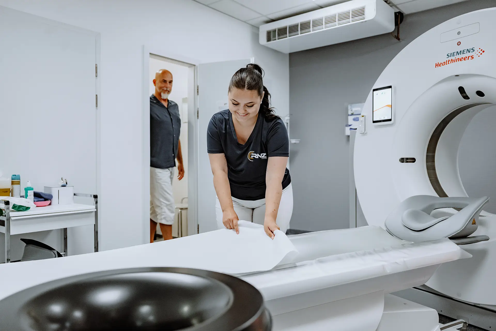 Medizinische Fachangestellte bereitet den Untersuchungstisch des Siemens-Computertomographen für einen Patienten vor.