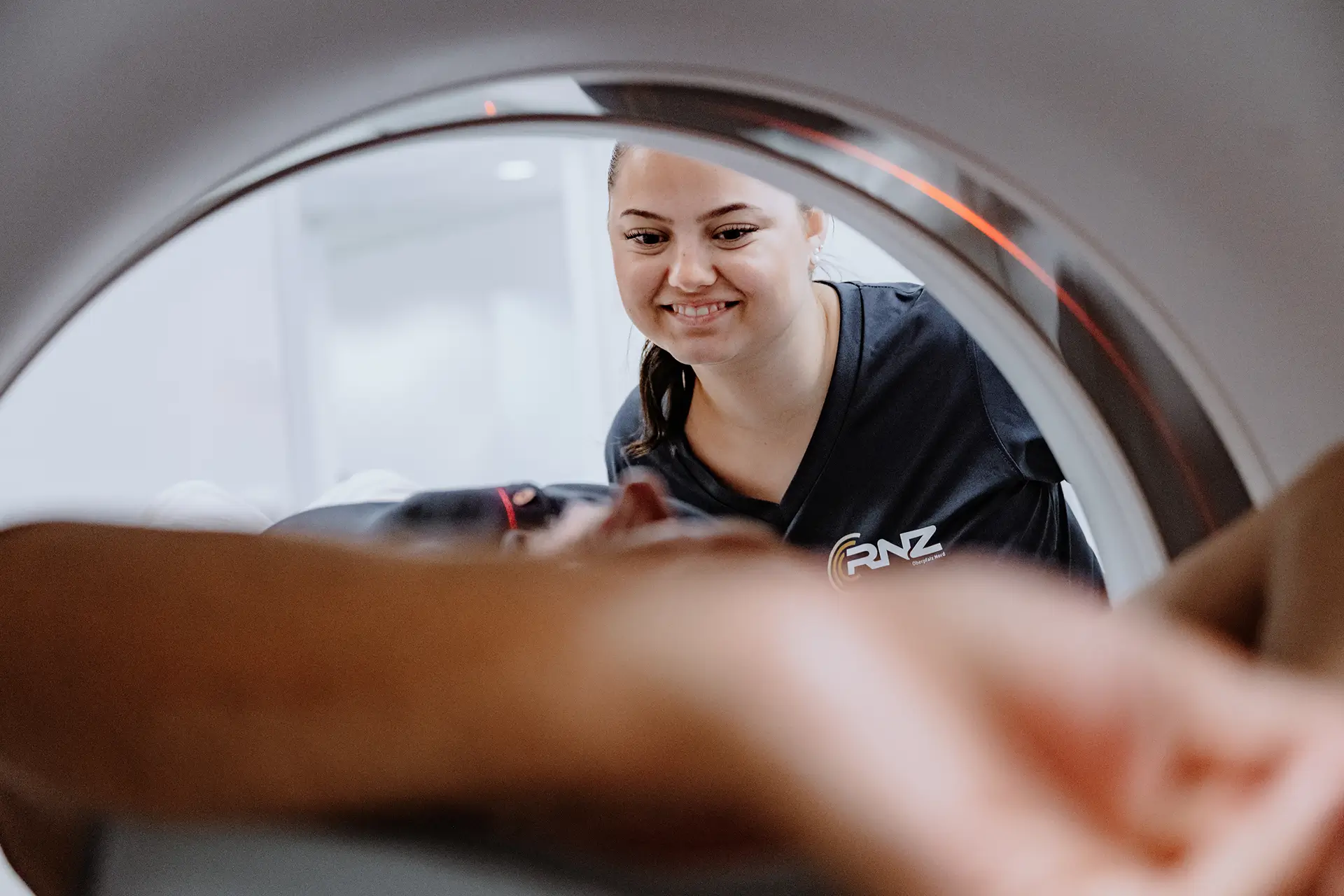 Medizinische Fachangestellte betreut einen Patienten durch die Öffnung des CT-Geräts während der Untersuchung.