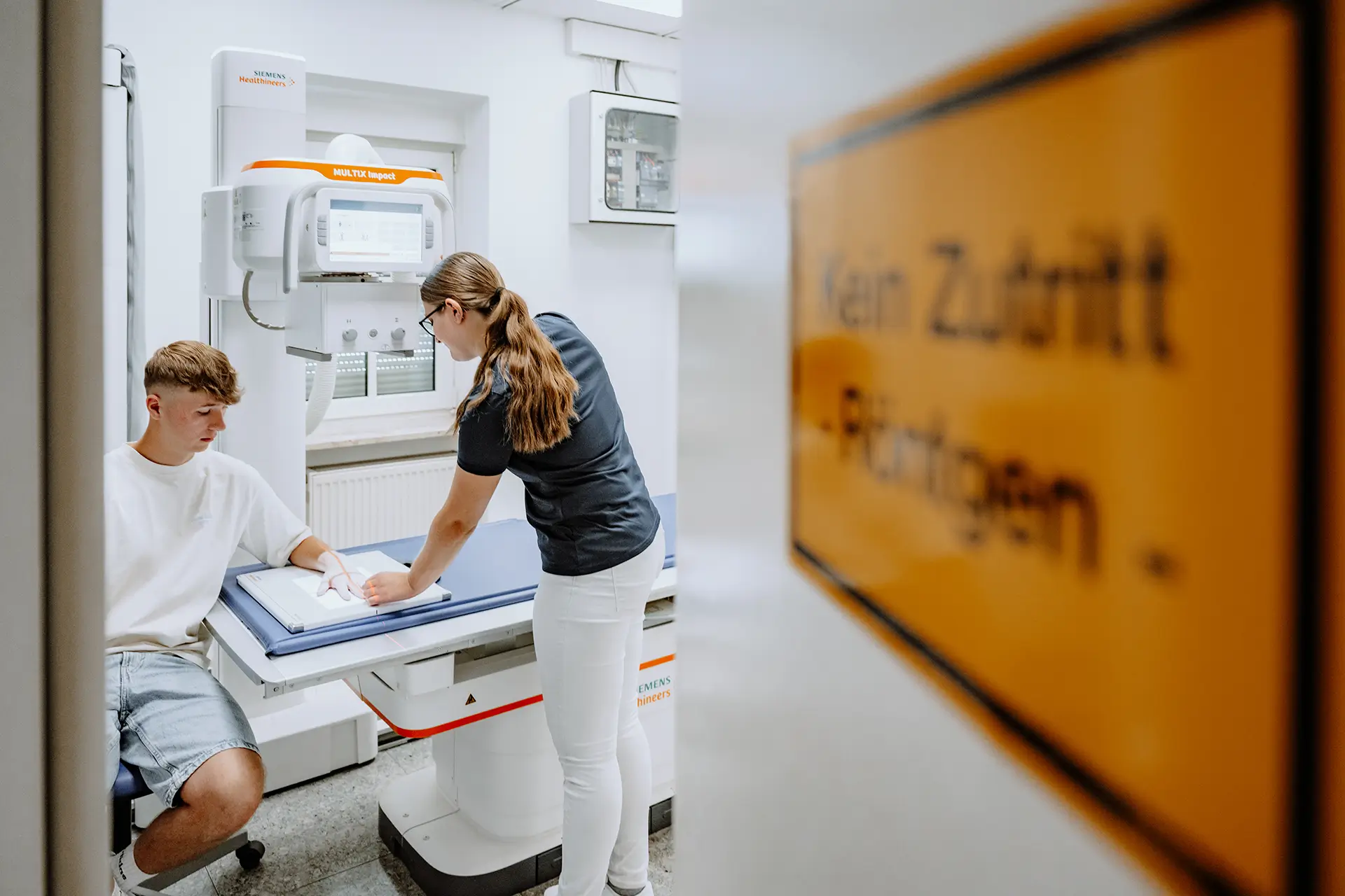 Medizinische Fachangestellte bereitet eine Röntgenaufnahme der Hand eines jungen Patienten vor.
