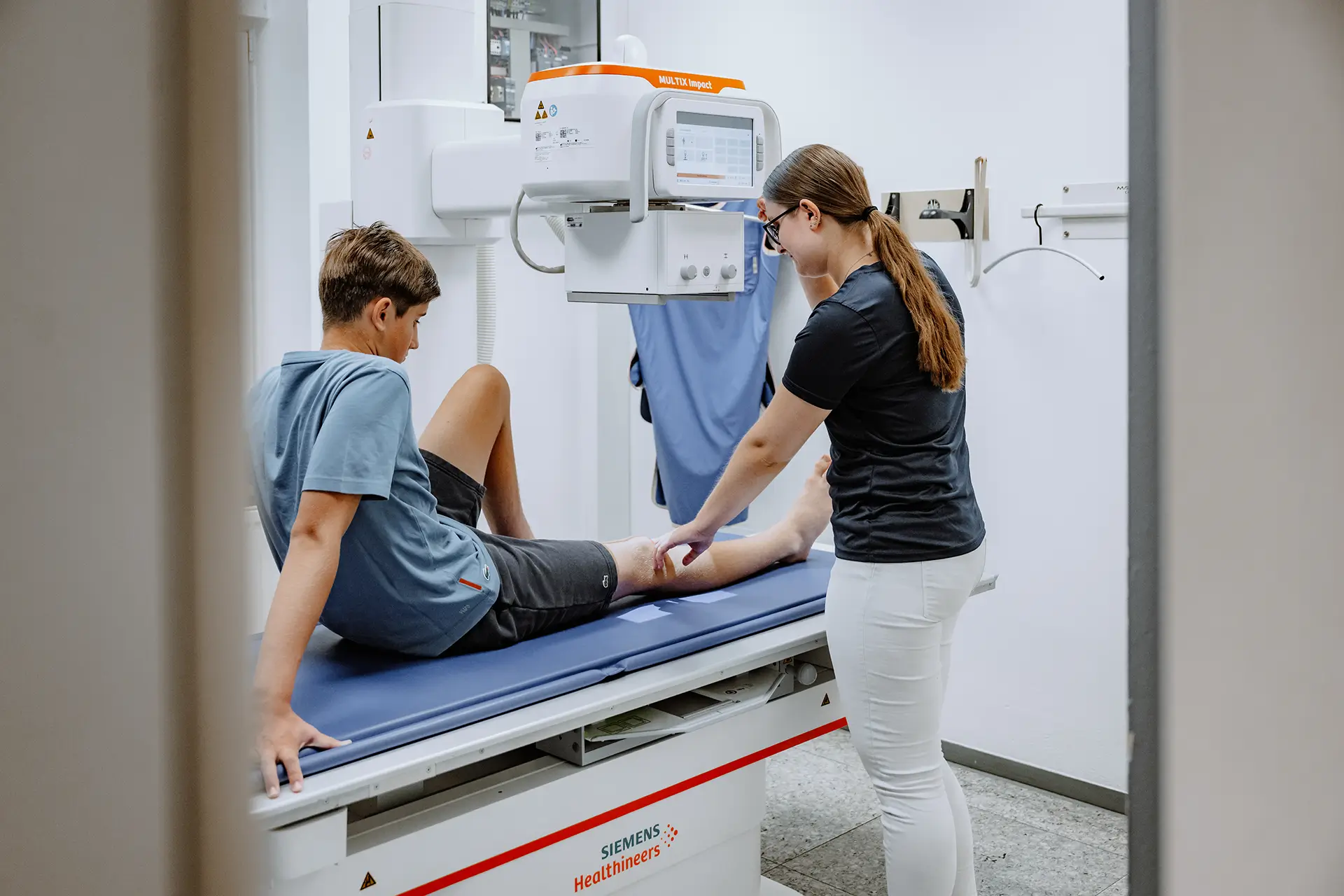 Medizinische Fachangestellte positioniert einen jungen Patienten für eine Röntgenuntersuchung am Siemens MULTIX Impact.